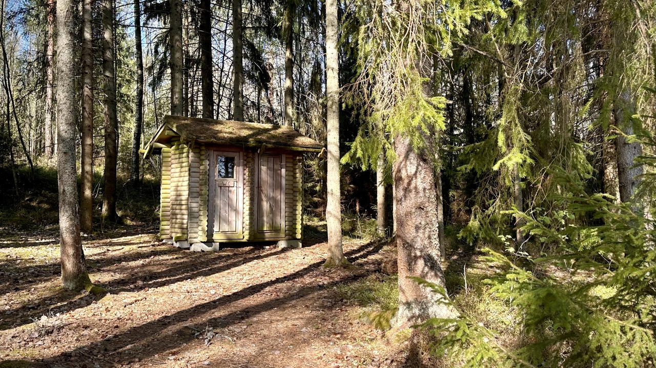 Hirsinen kaksiovinen rakennus metsässä.