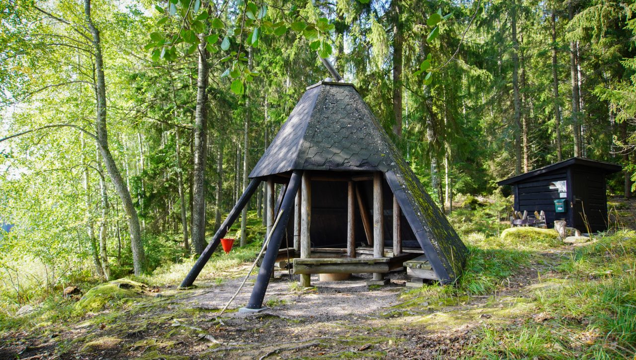 Suuri mustaksi maalattu kotalaavu, jonka takana on metsää.