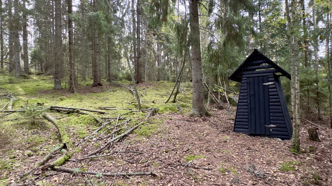 Black painted wooden dry toilet in the forest.