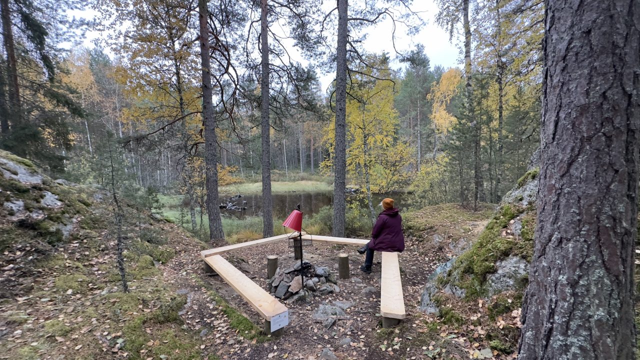 Nainen istuu nuotiolla ja katsoo järvelle.