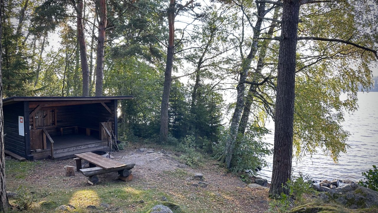 Tumma puinen laavu järven rannalla.