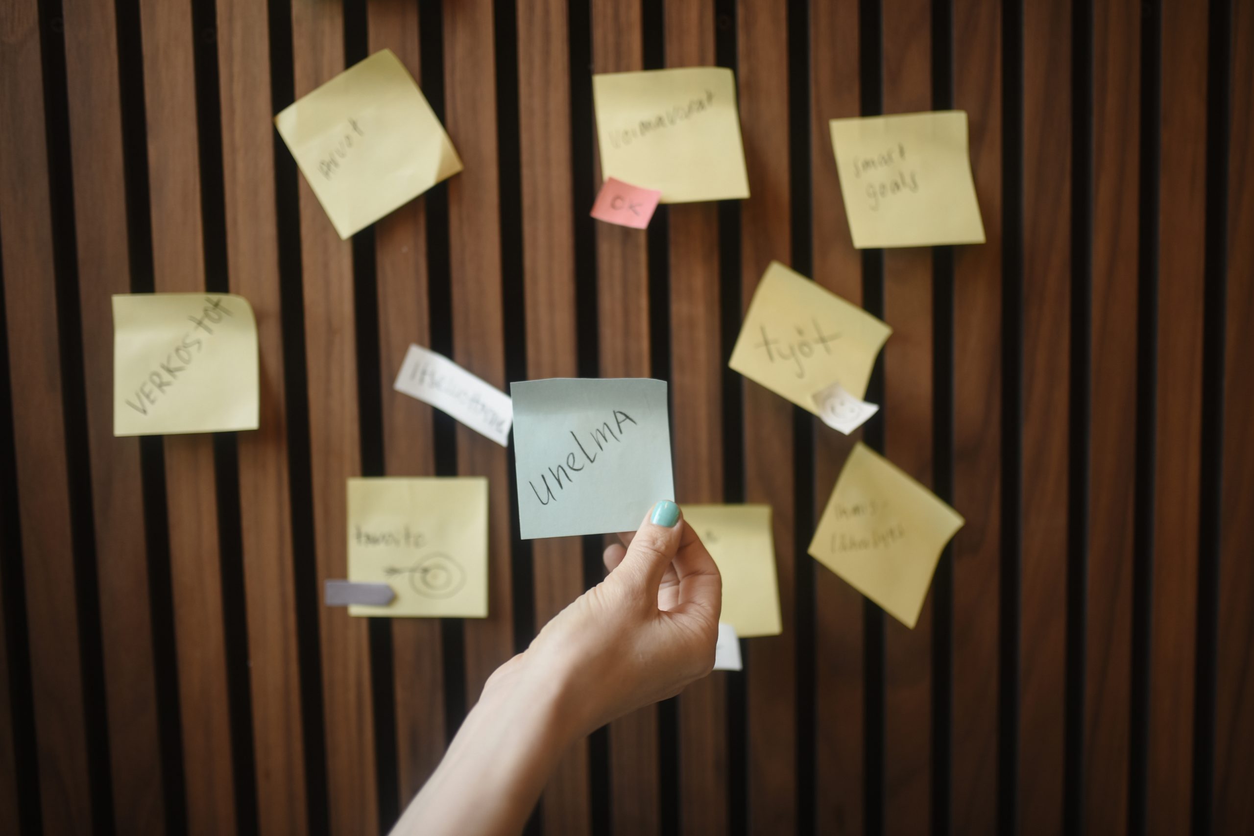 Post it -lappuja seinällä, keskiössä henkilön kädessä lappu, jossa tekstinä unelma.