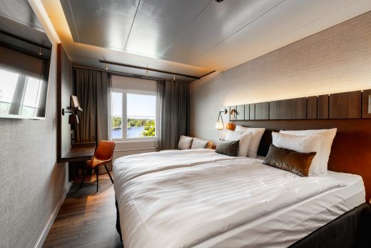 Kahdenhengen hotellihuone. Jalopuuta ja ikkunasta näkymä kesäiselle Vanajavedelle.