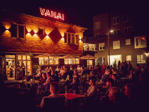 Vanain edustalta ilta-aikaan. Terassilla paljon ihmisiä ja rakennuksen valot valaisevat.
