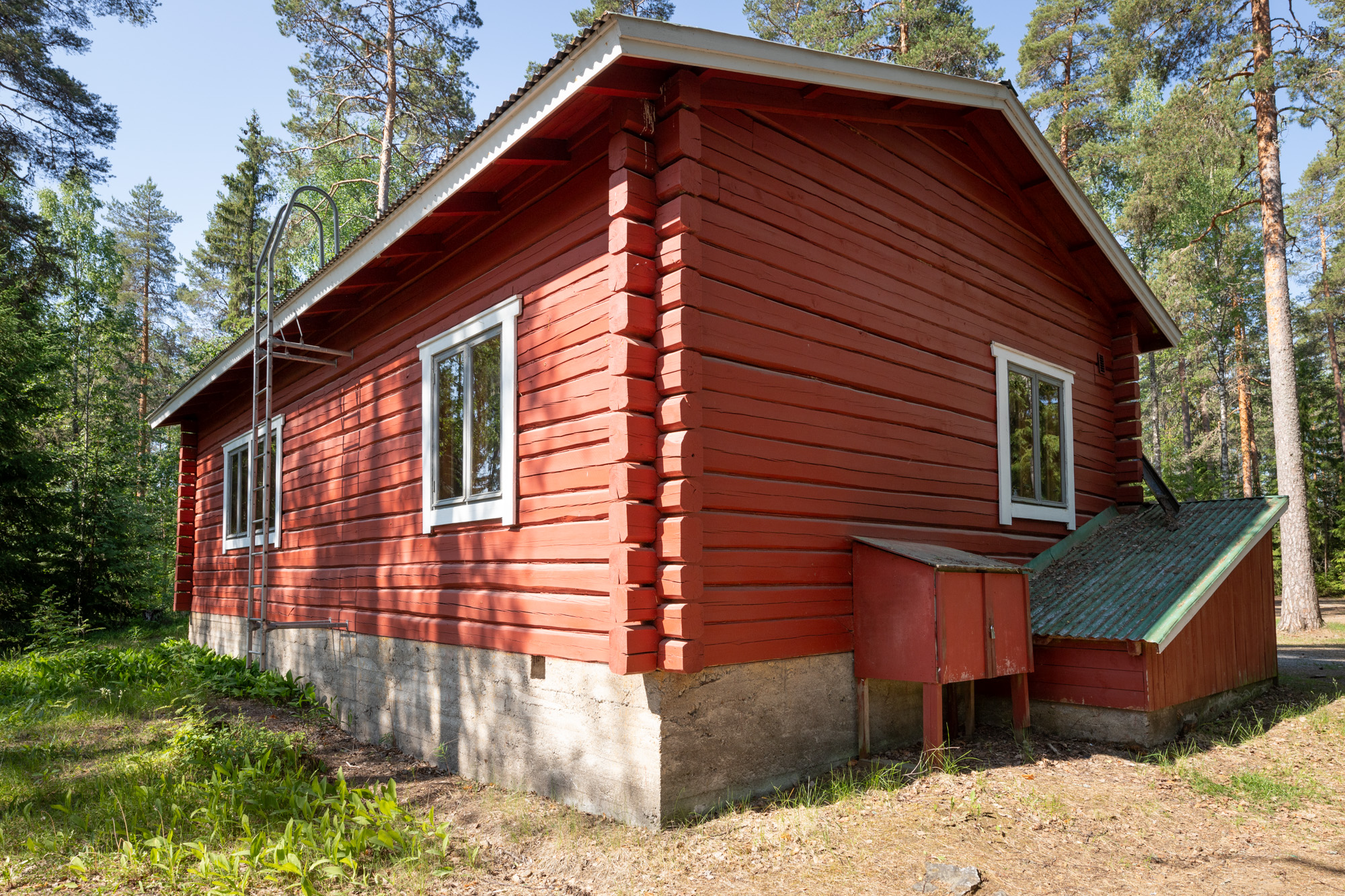 Edessä savottakämppä, joka on metsän keskellä
