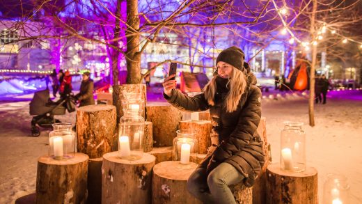 Talvinen kuva kaupungista kynttilöineen jossa henkilö ottaa itsestään kuvaa kännykällä.