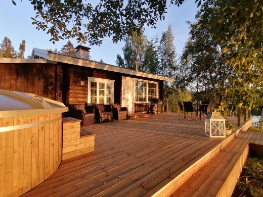 Sauna, puinen terassi ja palju kesäauringon laskun väreissä.
