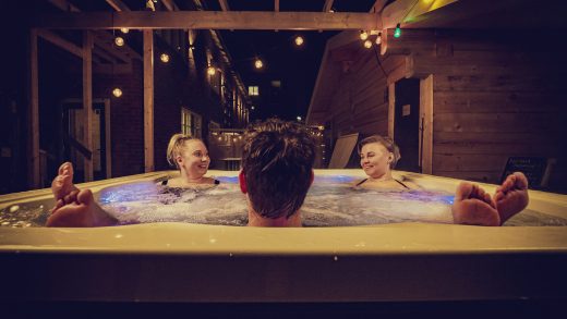 Kolme henkilöä poreissa ulkotiloissa. Roikkuvat valot valaisevat.
