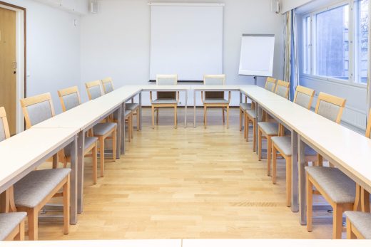 Kokoustila jossa pöydät U-muodossa. Takaseinällä valko- ja lehtiötaulu.