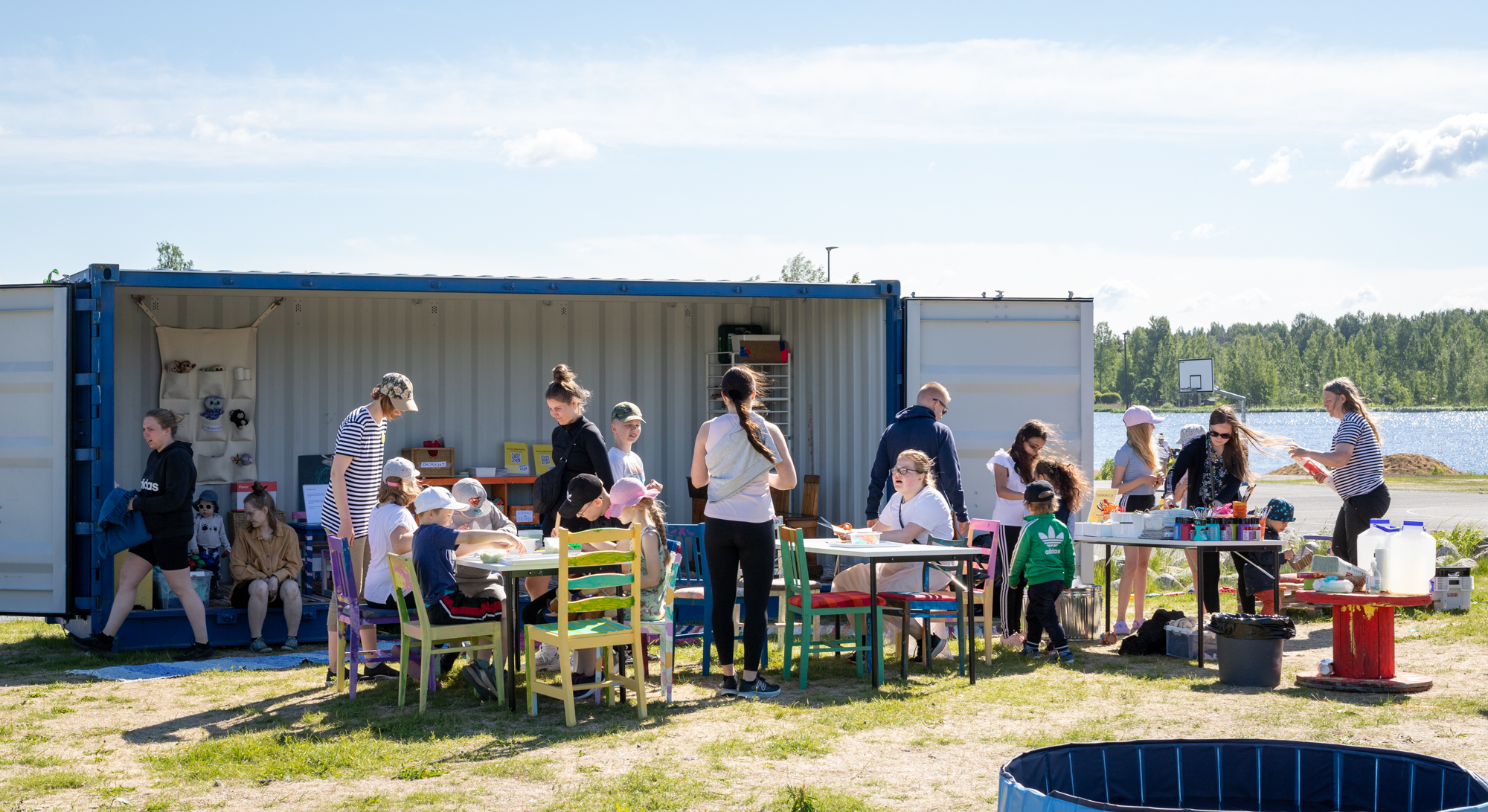 Ihmisiä ulkona istumassa pöytien ääressä osallistumassa taidetoimintaan.