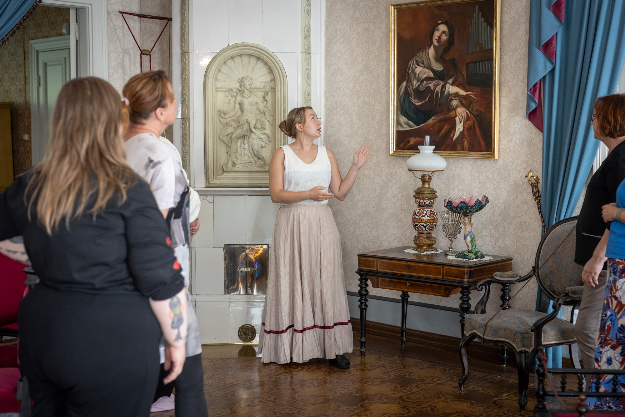 Ihmisiä talossa, joka on sisustettu 1800-luvun tyyliin. Yksi ihminen esittelee taulua muille.