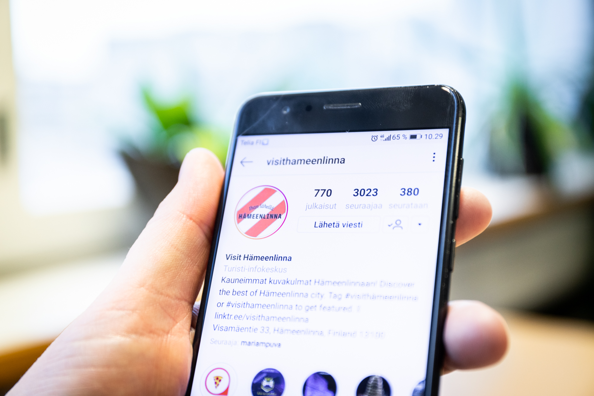 Henkilö pitää kädessään matkapuhelinta, jossa on avoinna VisitHämeenlinnan Instagram-tili.