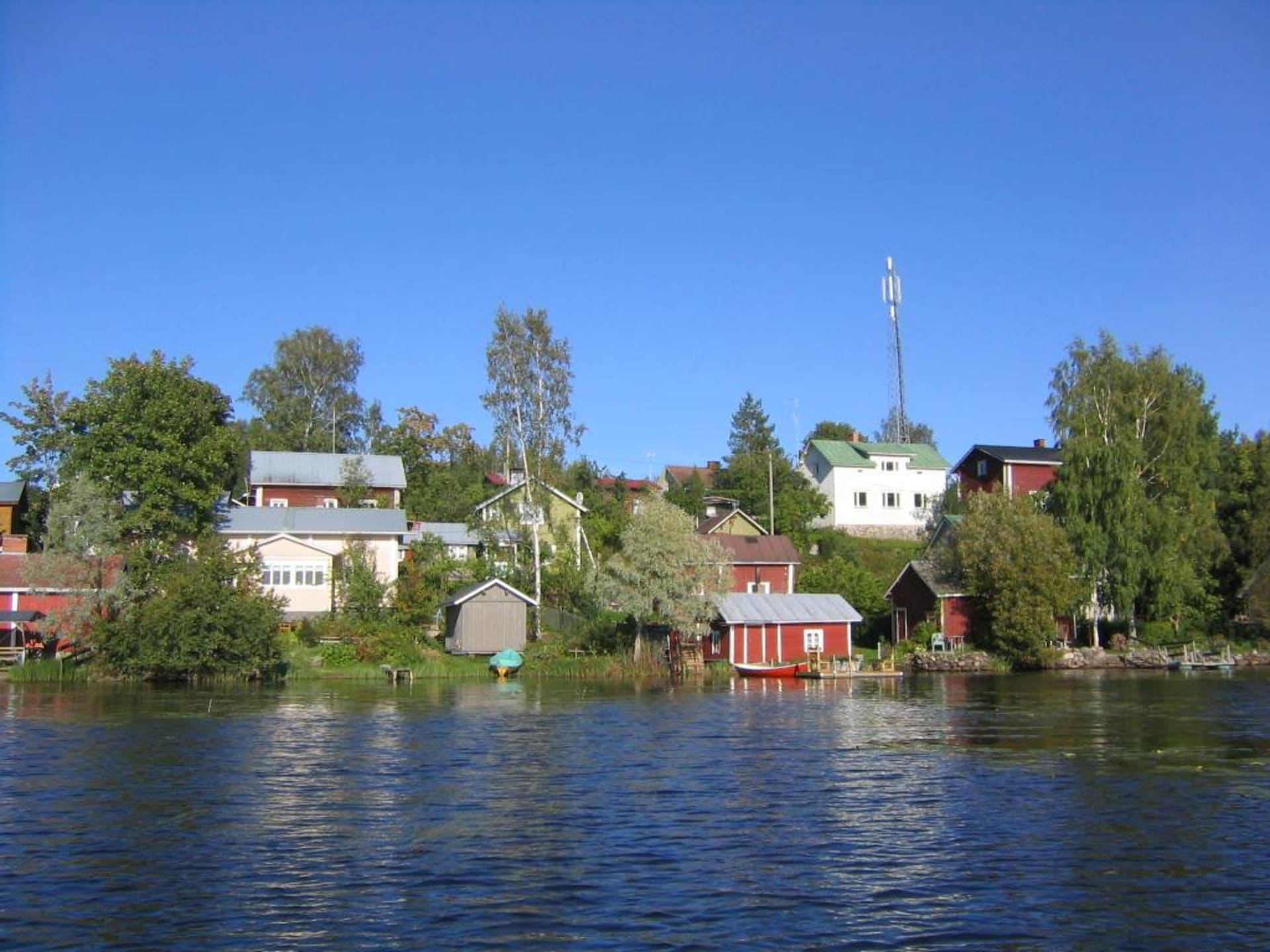 Kesäinen näkymä Hauhon Vanhalla raitilla, punainen puutalo, pihapiiri ja taustalla sinitaivas.