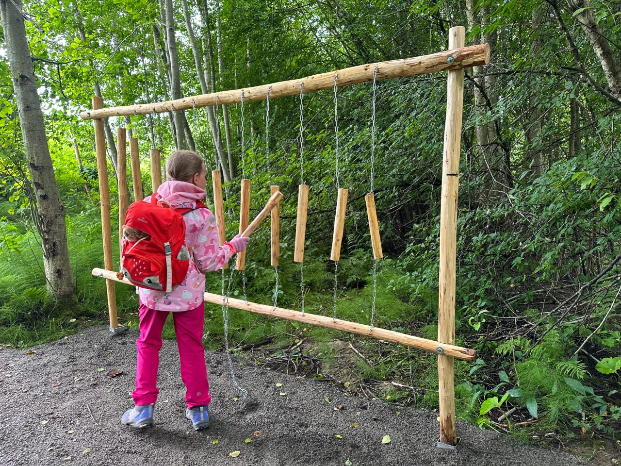 Lapsi soittaa isoa puusta tehtyä ksylofonia metsässä polun varrella.